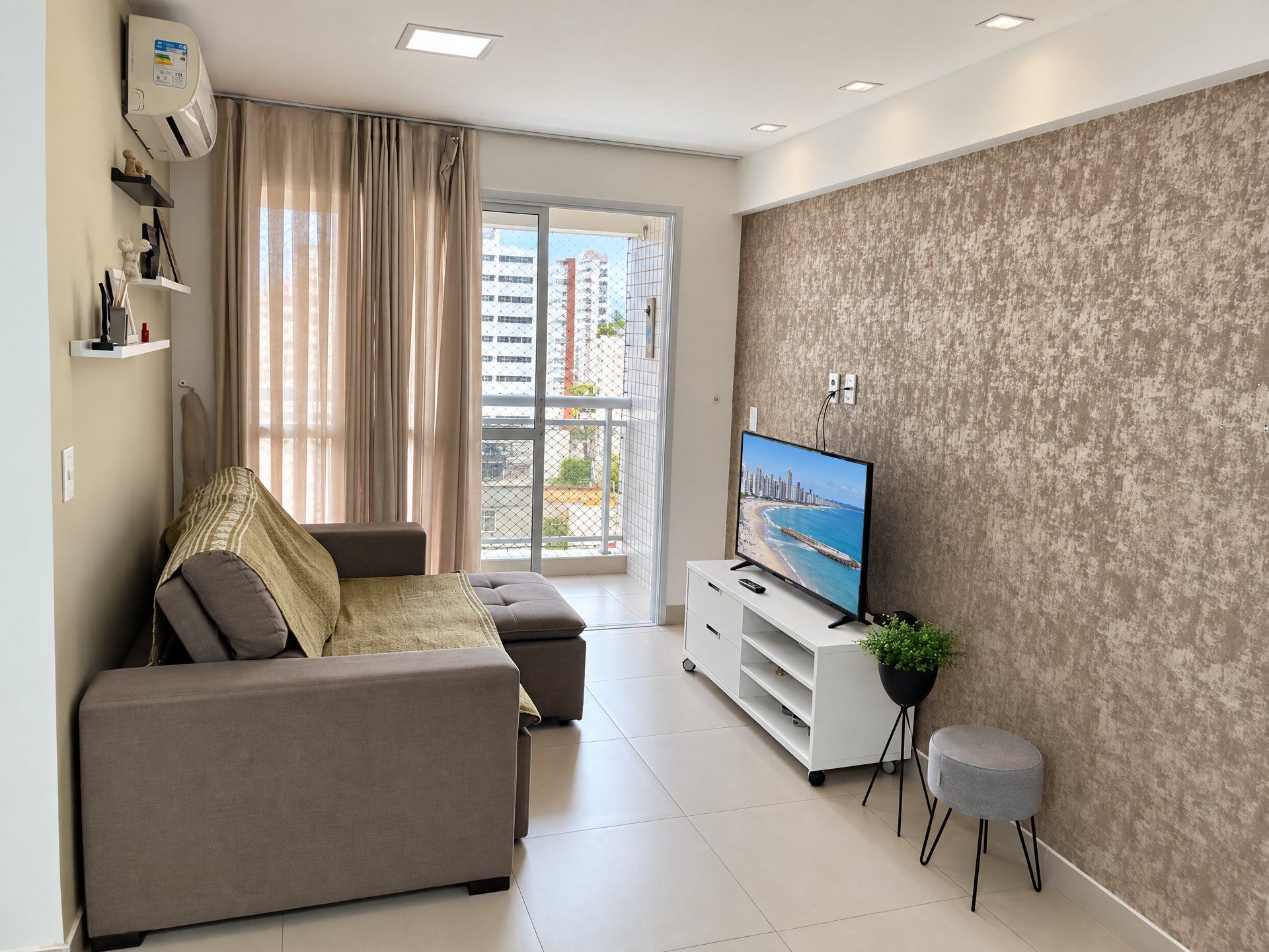 Uma sala de estar moderna com sofá, televisão e varanda com vista para a cidade.