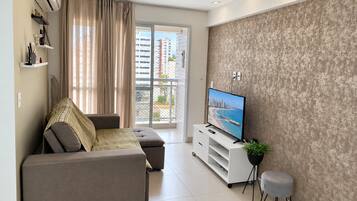 A modern living room with a sofa, a television, and a balcony with a city view.