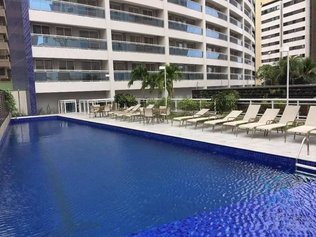 A hotel pool area with lounge chairs, a small table, and a palm tree.