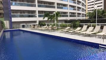 A hotel pool area with lounge chairs, a small table, and a palm tree.