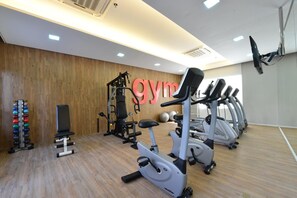 Une salle de sport équipée de matériel d’exercice, d’un climatiseur fixé au mur et d’un plancher en bois.