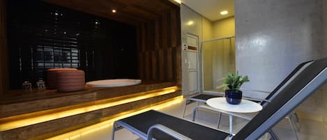 A modern bathroom with a wooden vanity, a bathtub, a shower, and a seating area with a table and chairs.