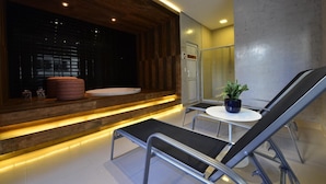 A modern bathroom with a wooden vanity, a bathtub, a shower, and a seating area with a table and chairs. - Flat 2 Quartos a 50m da Praia Perto da Feirinha (Fortaleza)