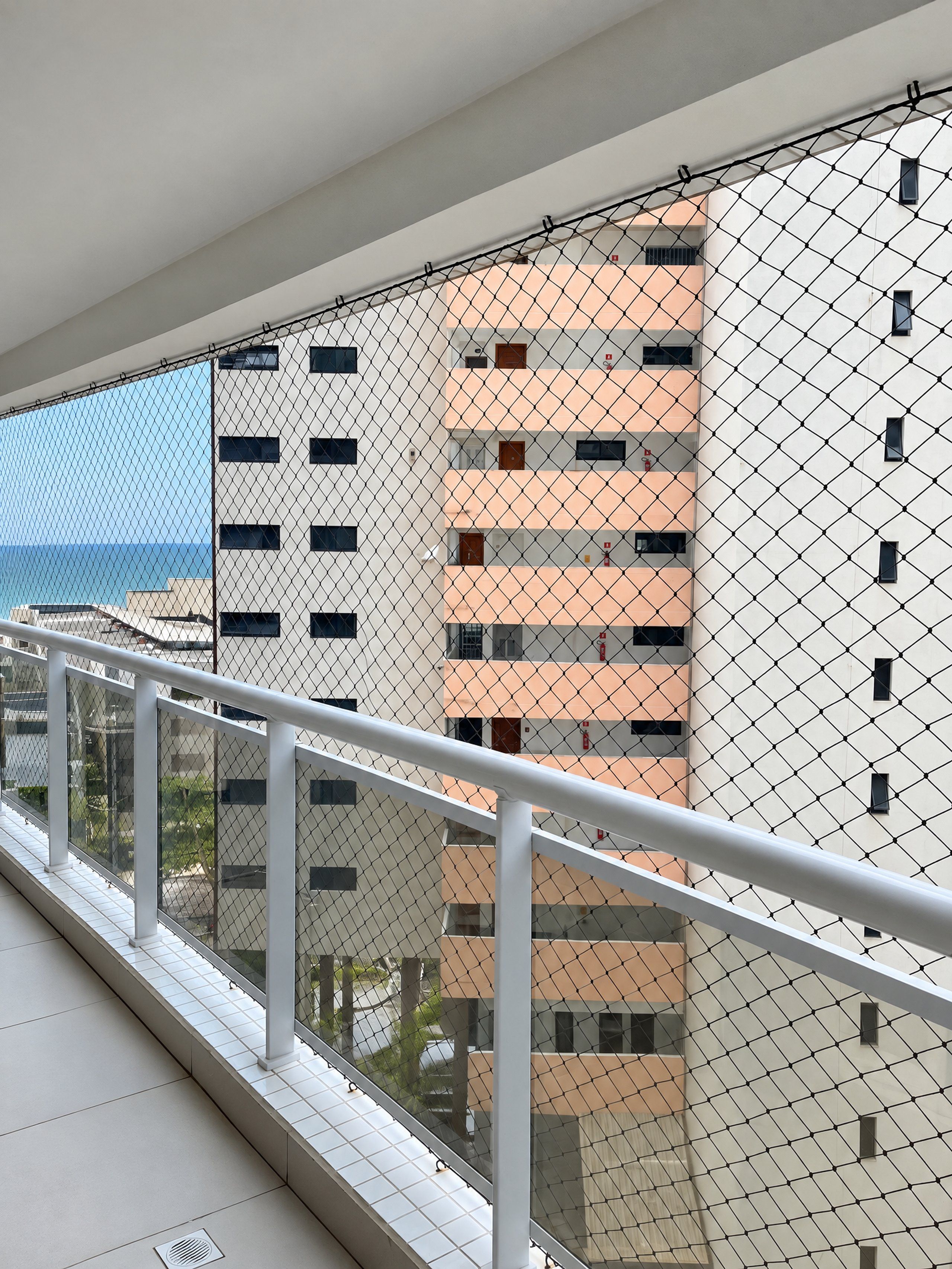 A balcony with a chain-link fence, overlooking a building with multiple floors and windows.