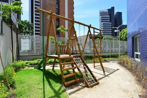 Ein Spielplatz mit einer Holzschaukel und Klettergerüst, umgeben von einer Rasenfläche und einem weißen Zaun.