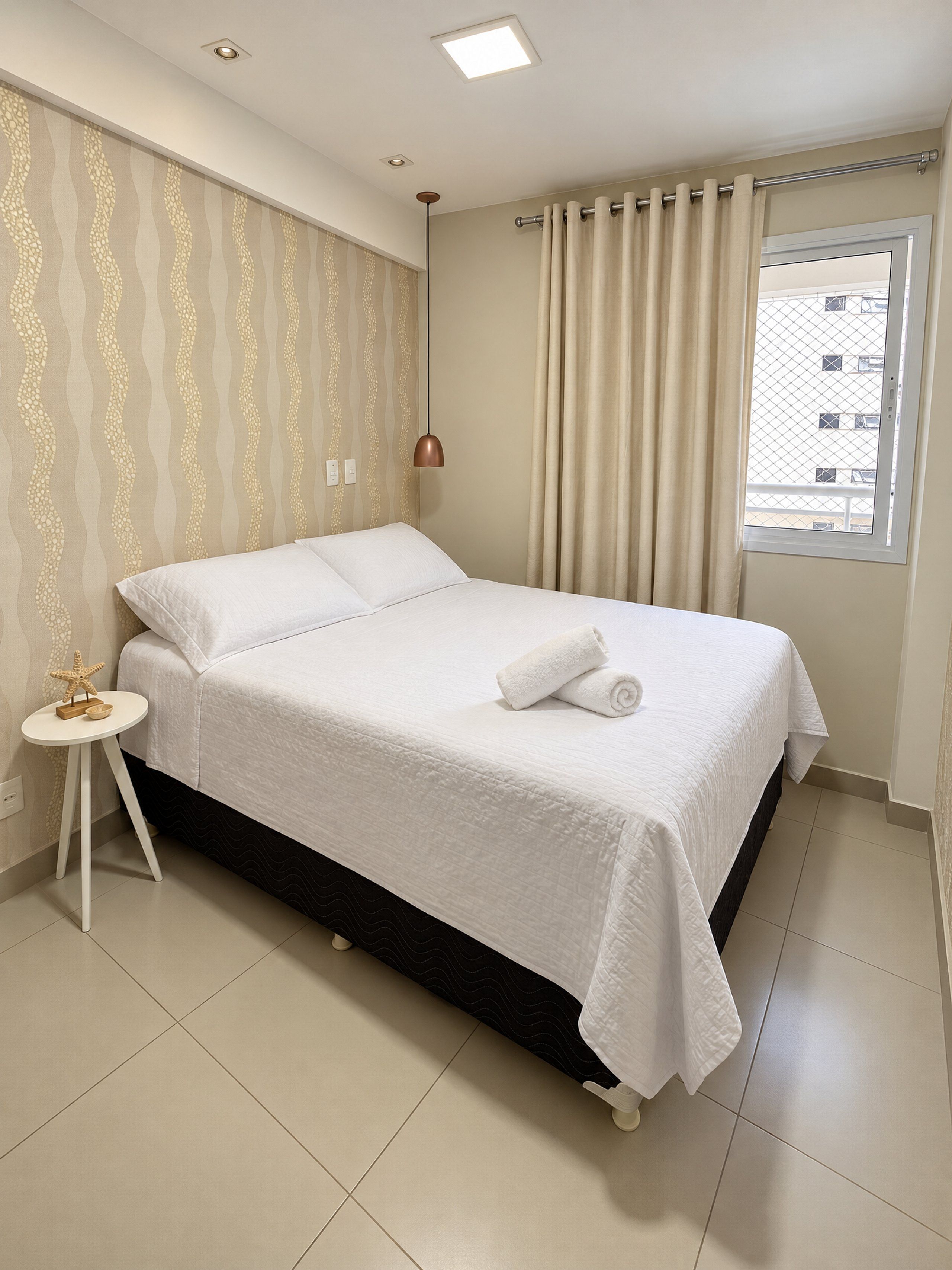 A neatly made bed with white linens, a small bedside table with a starfish decoration, and a window with curtains.