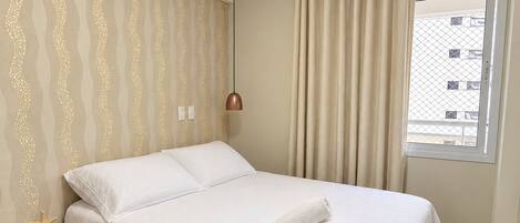 A neatly made bed with white linens, a small bedside table with a starfish decoration, and a window with curtains.