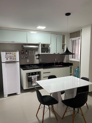 Eine moderne Küche mit einem weißen Kühlschrank, Herd, einer Mikrowelle und einem Esstisch mit Stühlen.
