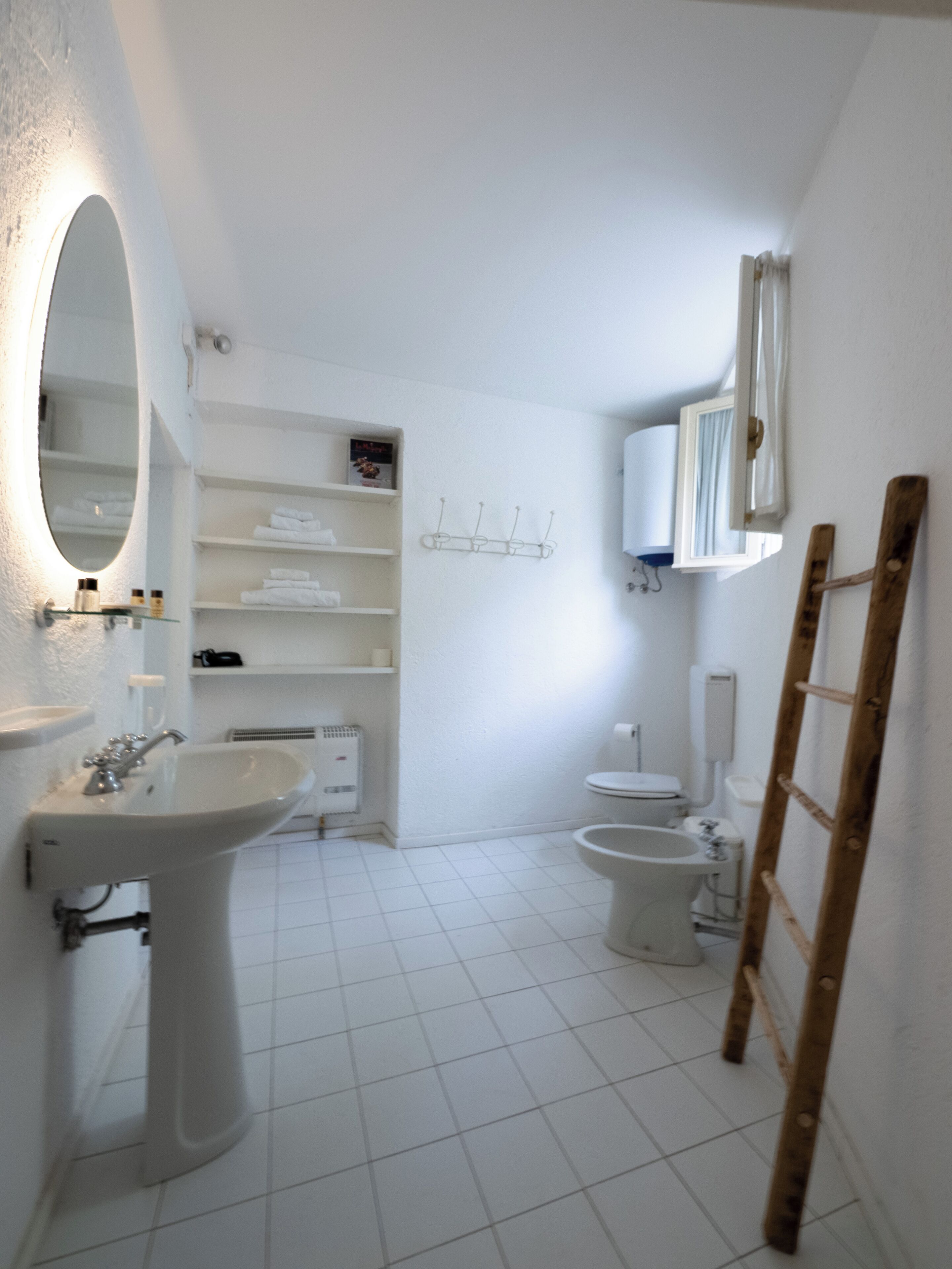 A bathroom with a pedestal sink, a mirror, a toilet, and a shower area.