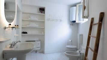 A bathroom with a pedestal sink, a mirror, a toilet, and a shower area.