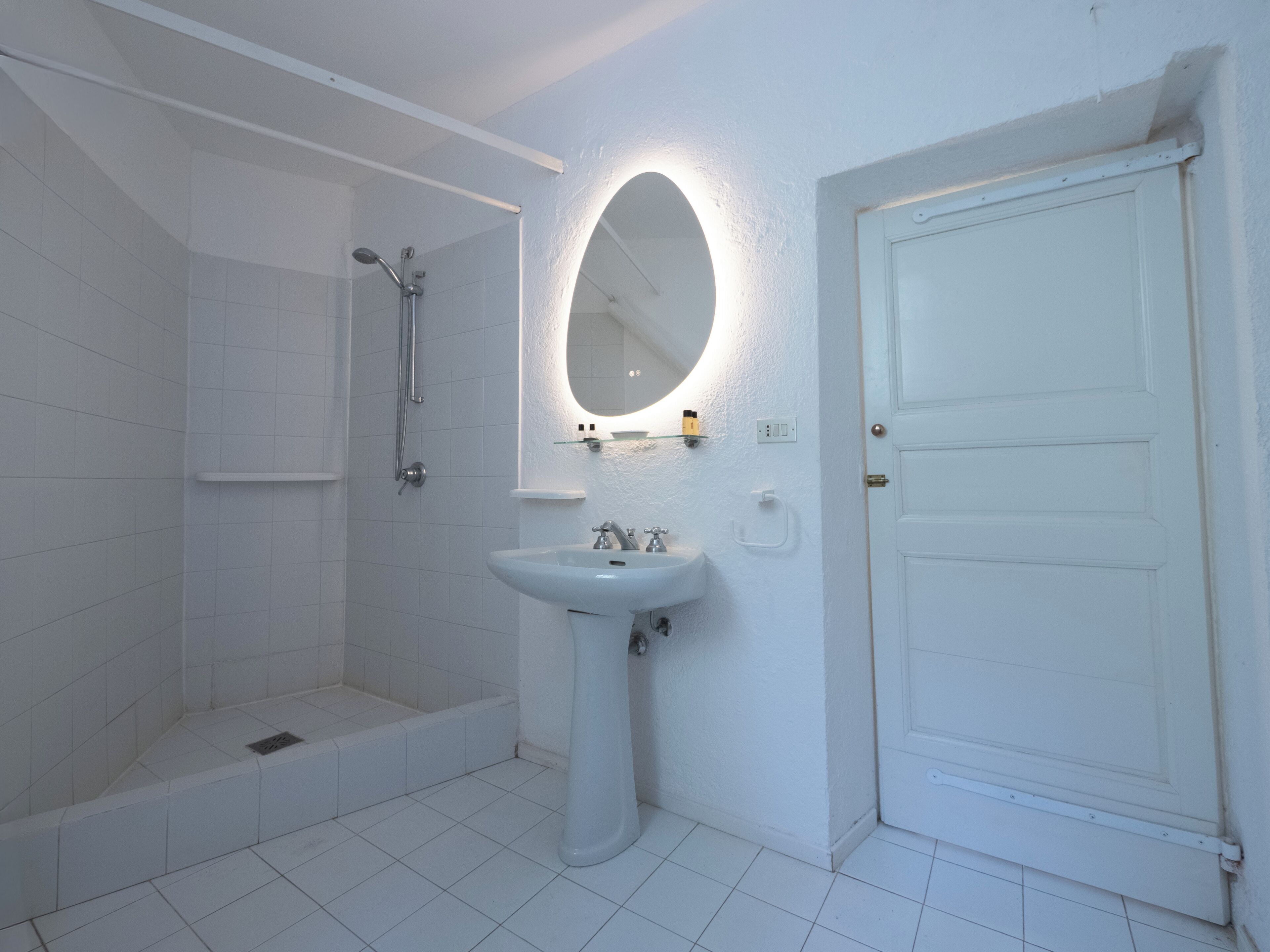 Un baño con lavamanos blanco, ducha y puerta.