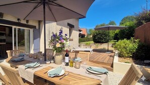 An outdoor dining area with wooden tables, chairs, and a large umbrella. - Les Embruns - 5-minute walk from the beach - Sleeps 10 - Villerville (Villerville)