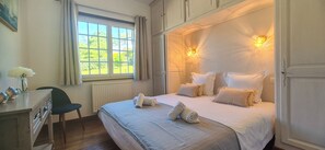 Ein Schlafzimmer mit einem Bett, Nachttischlampen, einem Fenster, einem Schreibtisch und einem Stuhl.