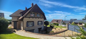Ein traditionelles Fachwerkhäuschen mit geneigtem Dach, einem eingezäunten Garten und freiem Blick auf das Meer.