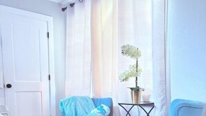 Ein Zimmer mit Holzboden, einer weißen Tür, zwei blauen Stühlen, einem kleinen Tisch mit einer Pflanze und einem Hund.