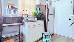 Eine kleine Küche mit Mikrowelle, Kaffeemaschine, Spüle und Kühlschrank.