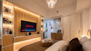 Une chambre d’hôtel moderne avec un grand lit, un téléviseur diffusant Netflix, une armoire en bois et un lustre.