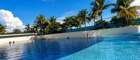 A clear blue pool with palm trees and a white wall in the background.