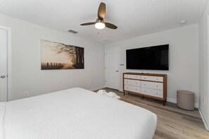 Een slaapkamer met een bed, een plafondventilator, een televisie, een dressoir en een schilderij aan de muur.