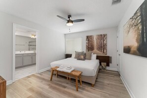 Ein Schlafzimmer mit einem Bett, einem Nachttisch mit Handtüchern, einem Deckenventilator und einem Bild an der Wand.