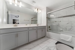 Een moderne badkamer met een grote spiegel, twee wastafels, een douche met glazen deuren en een marmeren vloer.