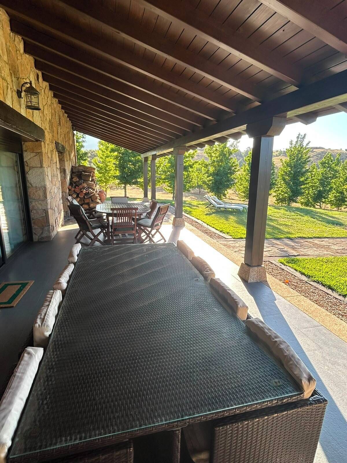 Une terrasse extérieure dotée d’un espace salon abrité, de murs en pierre et offrant une vue sur un jardin aménagé.