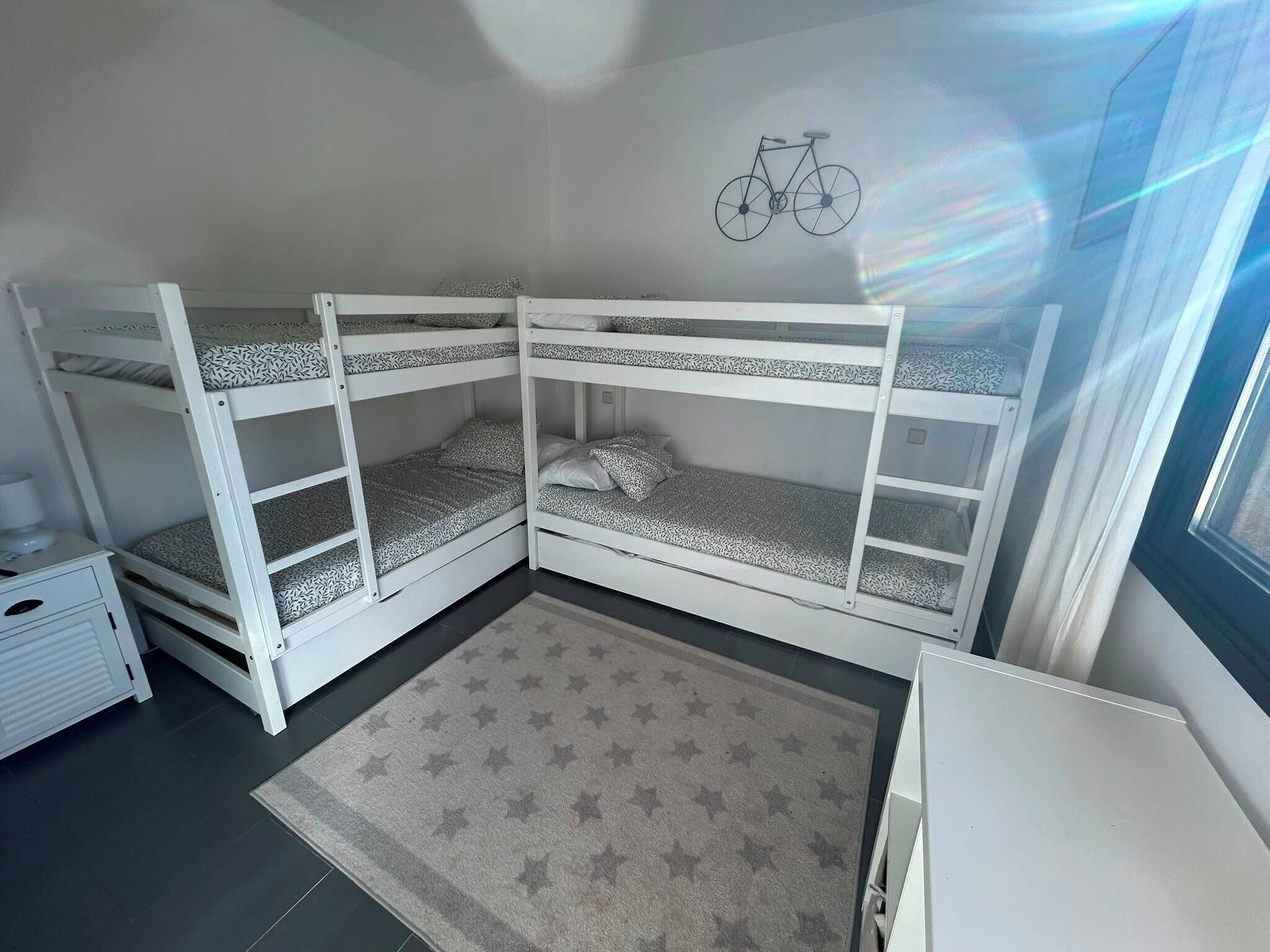 A bunk bed room with a star-patterned rug, a small bedside table, and a bicycle wall decoration.