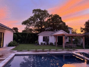 Ein Garten mit Pool, einem kleinen Haus und einem großen Baum.