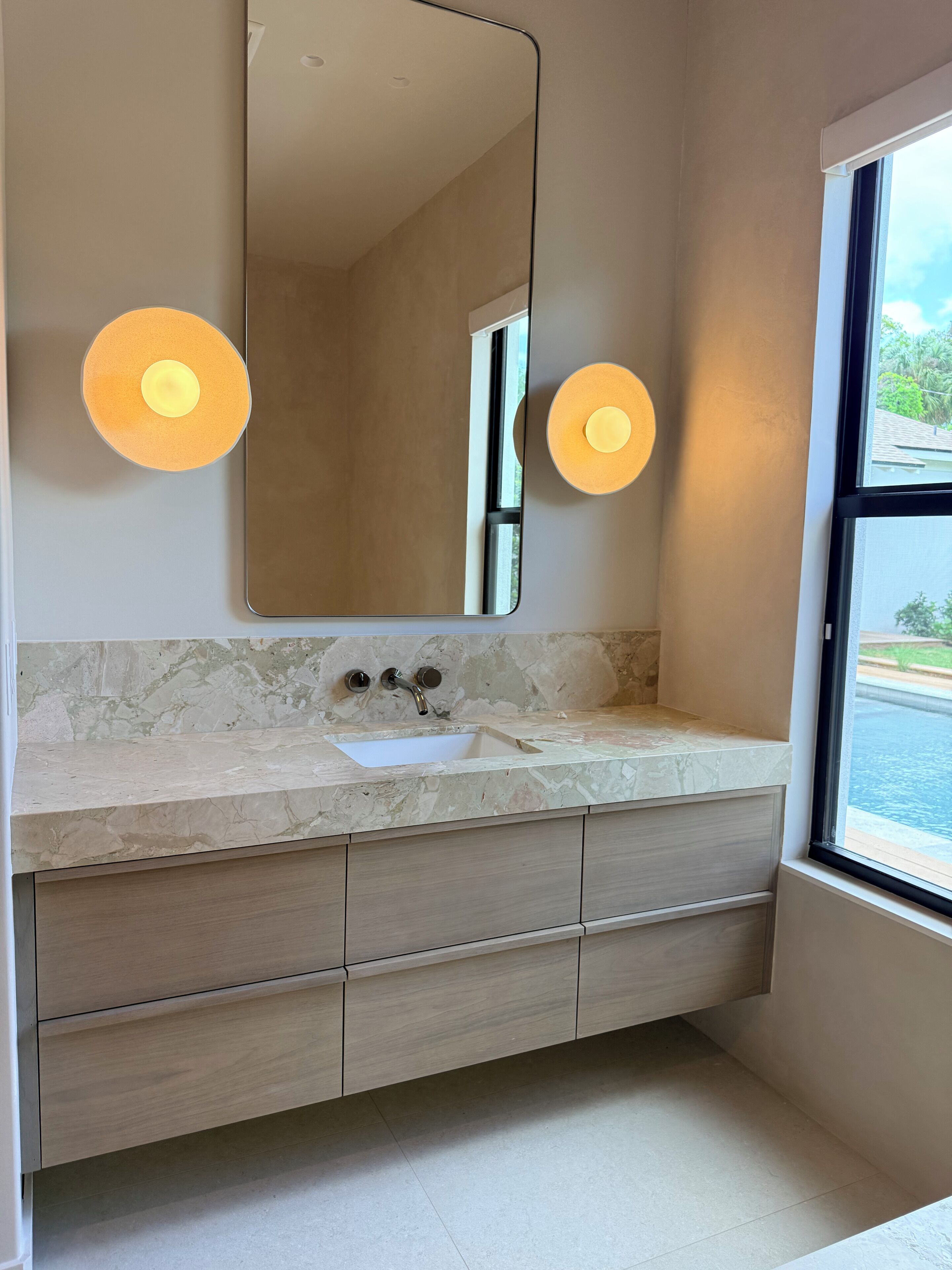 A bathroom with a marble countertop, a sink, a mirror, and two wall-mounted lights.