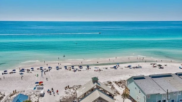 Een strand met helder turquoise water, een zandstrand en verschillende parasols en ligstoelen.