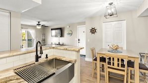 Een moderne keuken met een inbouwspoelbak, een eethoek met een houten tafel en stoelen, en een plafondventilator.