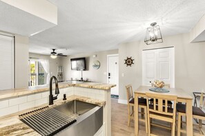 Eine moderne Küche mit integriertem Spülbecken, einem Essbereich mit Holztisch und Stühlen sowie einem Deckenventilator.