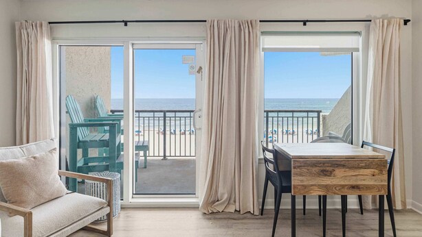 Ein Zimmer mit Balkon, einem Esstisch, Stühlen, einer Couch und Blick auf den Strand.