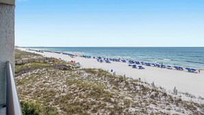Ein Strand mit weißem Sand, blauen Sonnenschirmen und einem klaren Himmel.