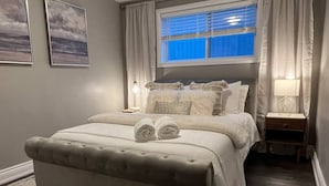 Ein Schlafzimmer mit einem großen Bett, einem Nachttisch, einer Lampe und einem Fenster mit Vorhängen.