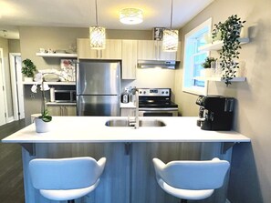 Une cuisine moderne dotée d’un îlot central, d’appareils électroménagers en acier inoxydable et de tabourets de bar blancs.