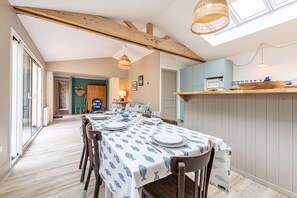 Ein Essbereich mit einem Tisch für vier Personen, Holzbalken an der Decke und einer Küchenzeile mit einer Mikrowelle und einer Holtschüssel auf der Arbeitsfläche.