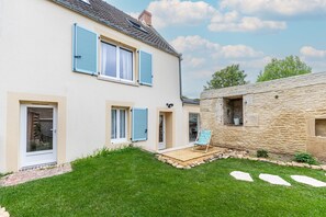 Ein zweistöckiges Haus mit einer Steinmauer, einer Holzterrasse und einem Rasen.