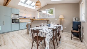 Een moderne keuken met dakramen, een eethoek met een tafel gedekt voor vier personen, en een kleine koelkast.