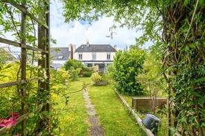 Ein Gartenweg führt zu einem Haus im traditionellen Stil, umgeben von üppiger Vegetation und einem Holzzaun.