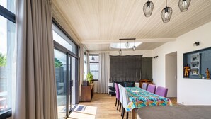 Un interior moderno con zona de comedor, un sofá y un amplio ventanal con cortinas.