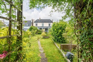 Ein Gartenweg führt zu einem Haus mit Holzzaun und viel Grün.