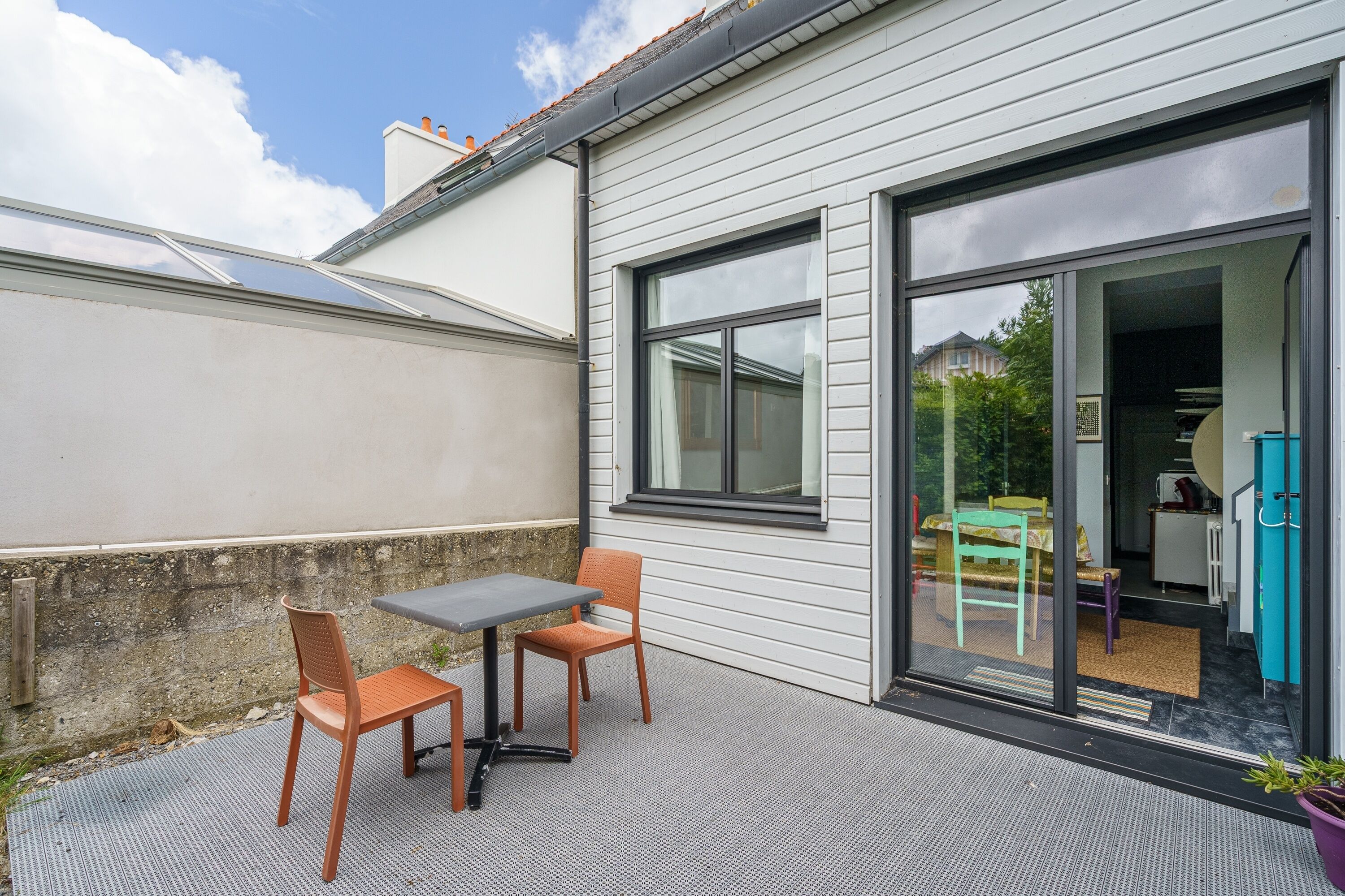 A patio with a table and chairs, a sliding glass door leading to an interior space, and a view of a neighboring house.