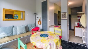 Um espaço compacto com sofá, pequena mesa de jantar, cadeira, espelho e cozinha compacta.