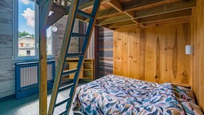 Um quarto com cama, paredes de madeira, uma escada, janela e radiador.