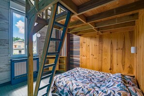 Ein Zimmer mit Bett, Holzwänden, einer Leiter, einem Fenster und einer Heizung.