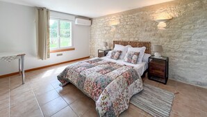 Un dormitorio con pared de piedra, cama con cubrecama floral, lámparas de noche y ventana con cortinas.