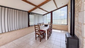 Un área de comedor con mesa y sillas, una pared de piedra y un ventanal con persianas.