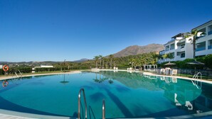 En swimmingpool med kristallklart blått vatten, omgiven av ett trädäck, med utsikt över ett bergigt landskap.