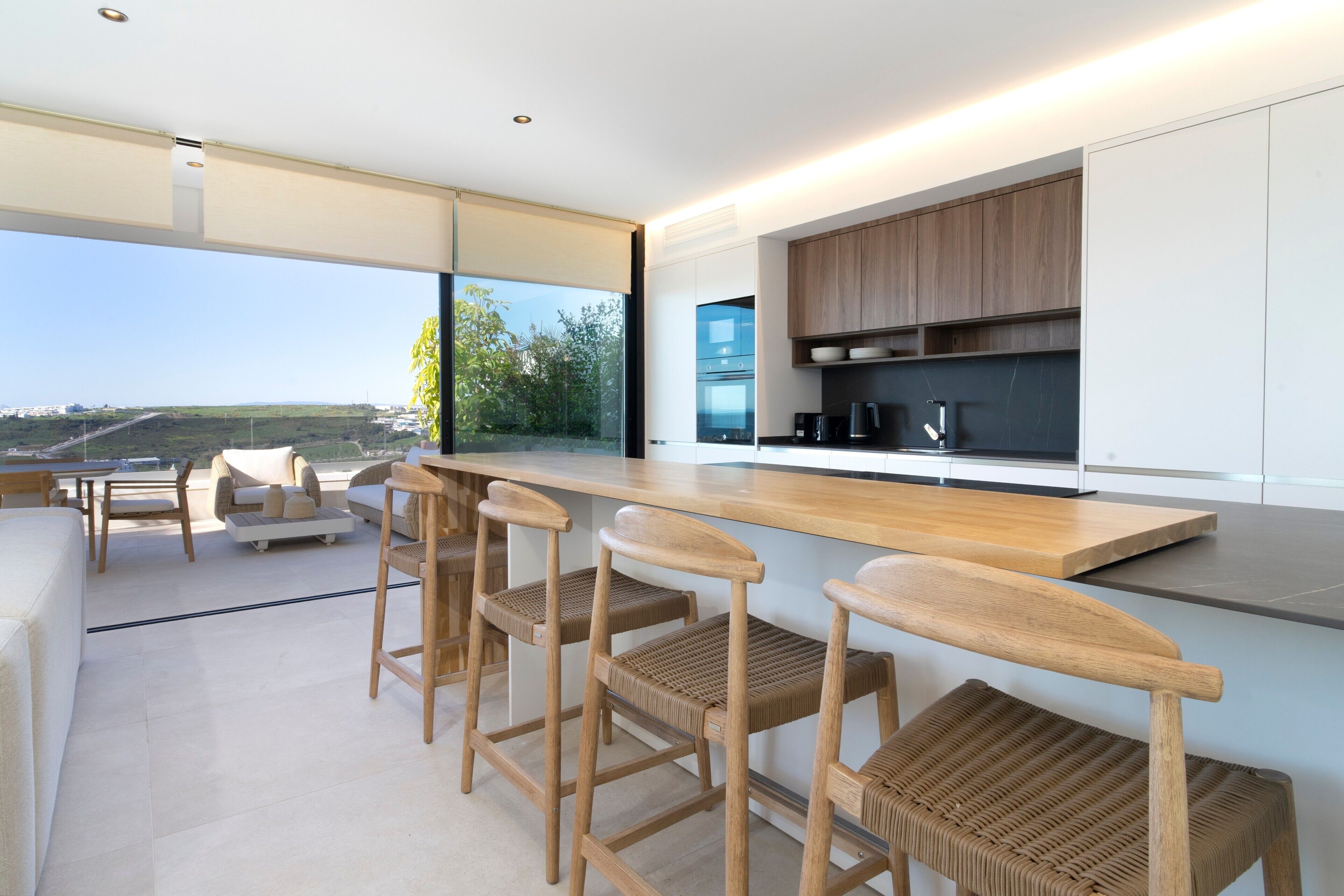 Een moderne keuken met houten barstoelen, een groot raam en uitzicht op het landschap.